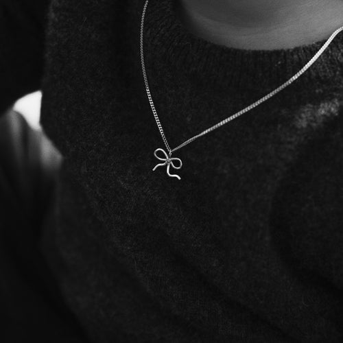 Silver bow necklace worn over a black knit sweater