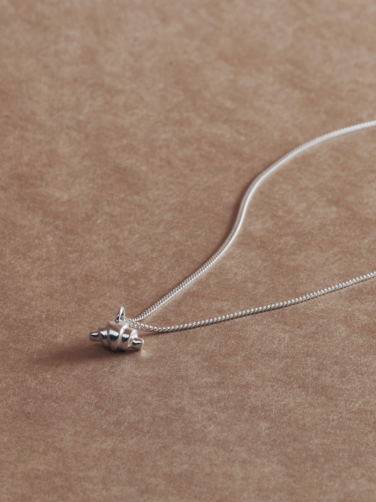 Silver croissant necklace on brown paper